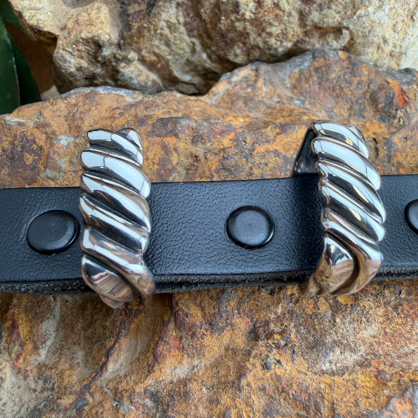Black leather belt with silver metal buckle on a stone background