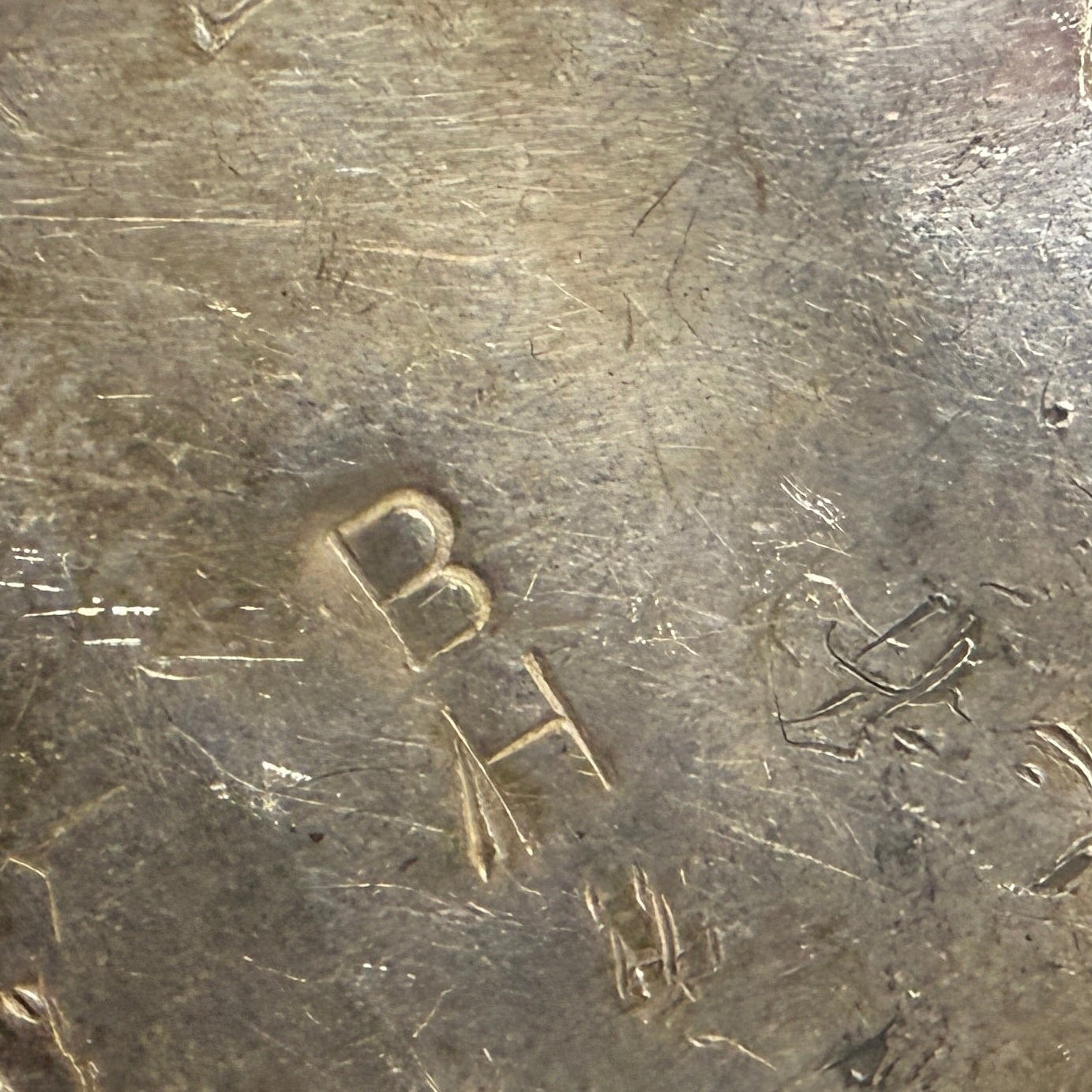A close-up of a worn metal object with engraved hallmark "BH"