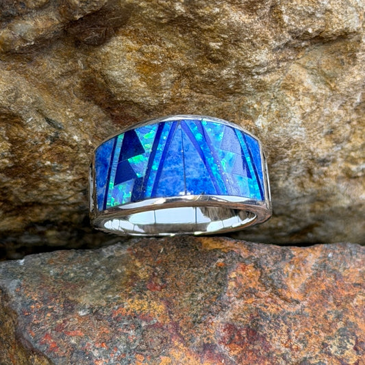 David Rosales Sterling Silver Ring with Inlaid Multicolored blue stones. Its inlay contains dark blue, light blue, and a blue opal. It rests on a rock surface.