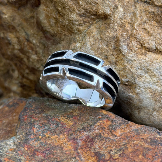 A silver-toned geometric ring with black details, resting on textured brown and orange rocks.