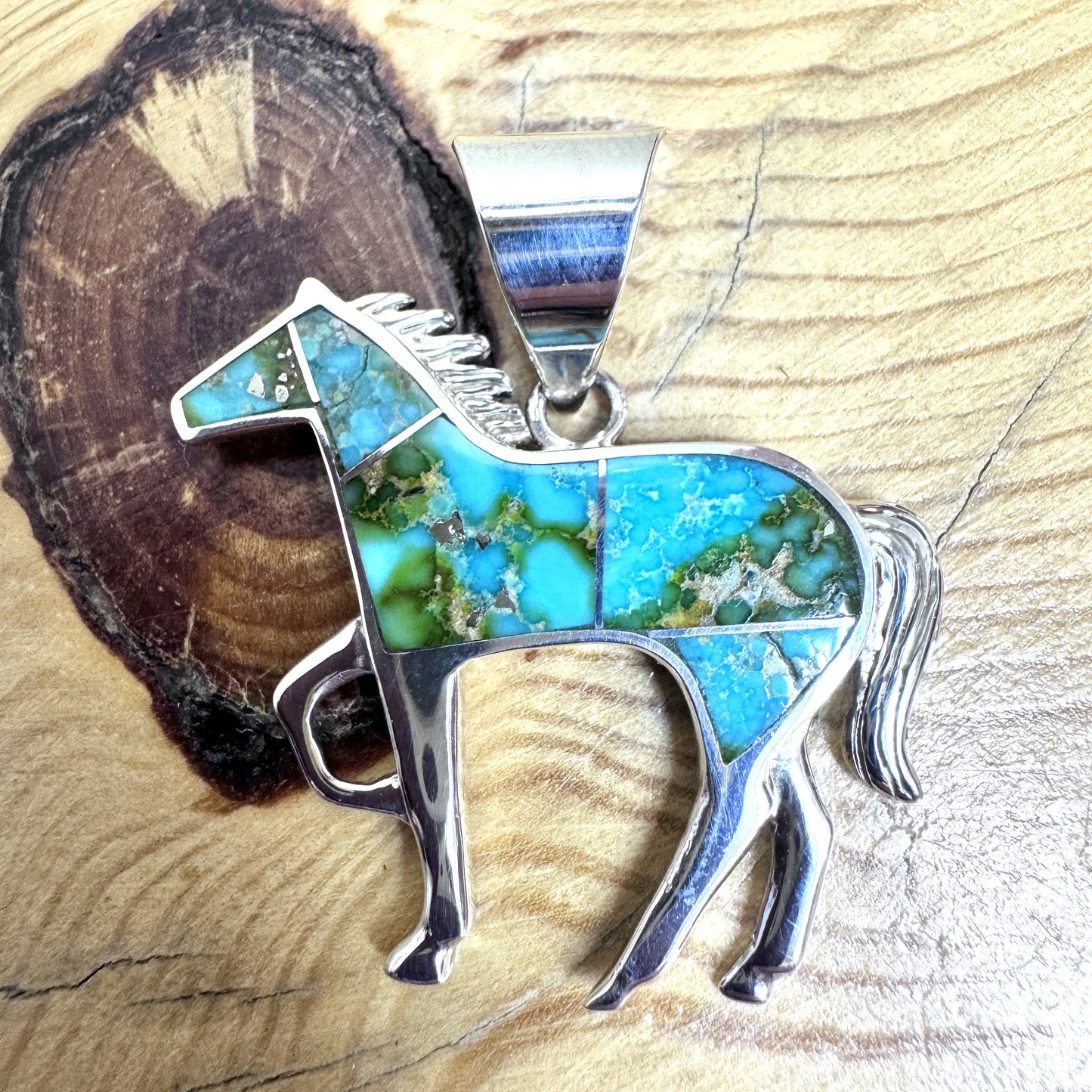 Turquoise and silver horse-shaped pendant on a wooden background