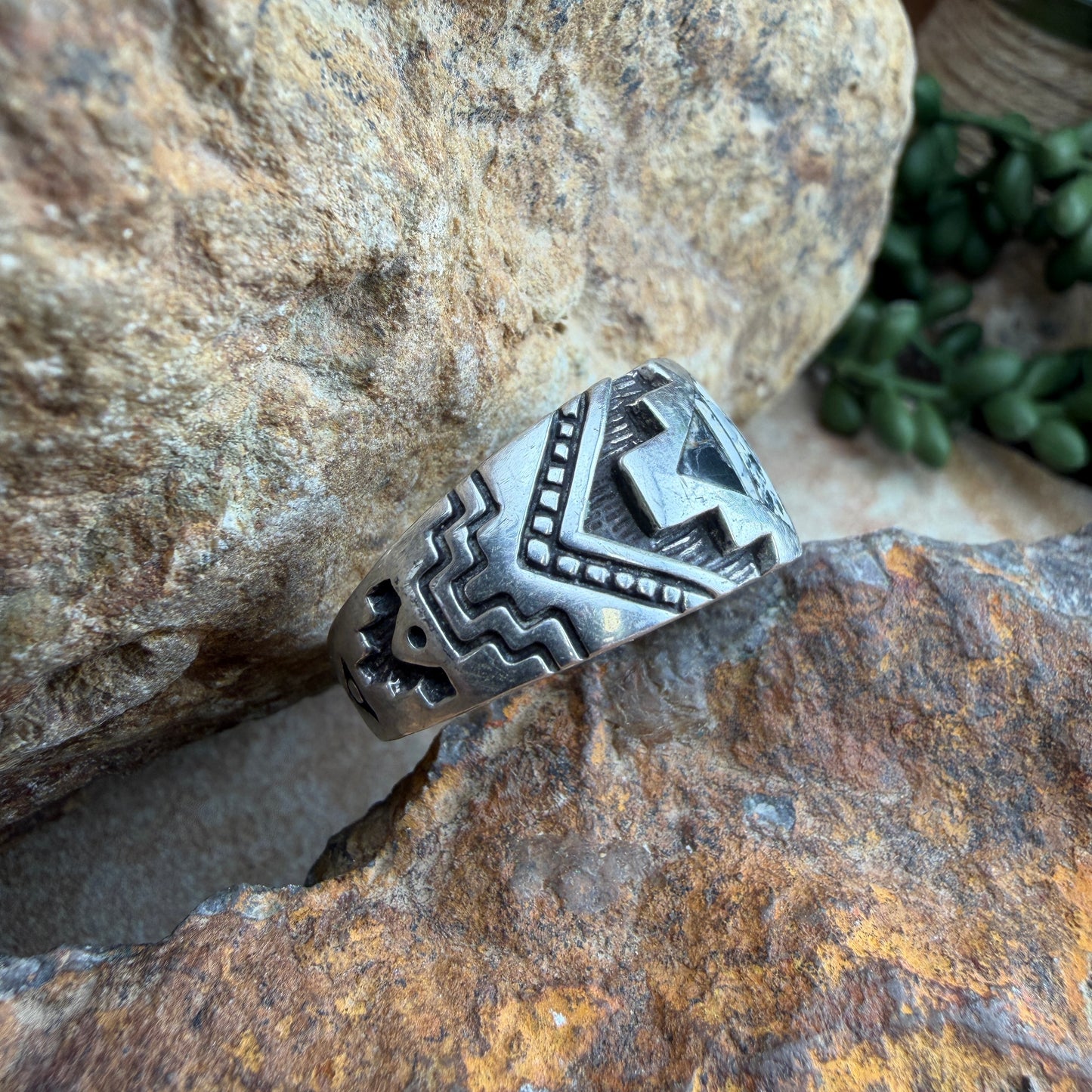 Silver ring with white and black inlay set in geometric design that is then stamped around the band with further details.