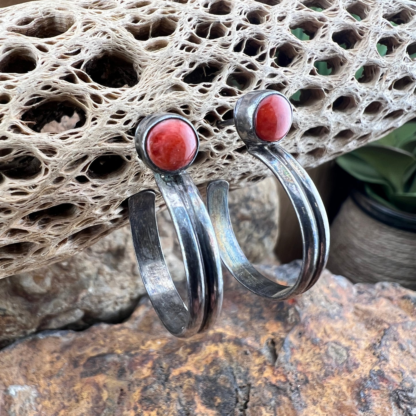 Silver hoop earrings with orange stones on a textured stone surface