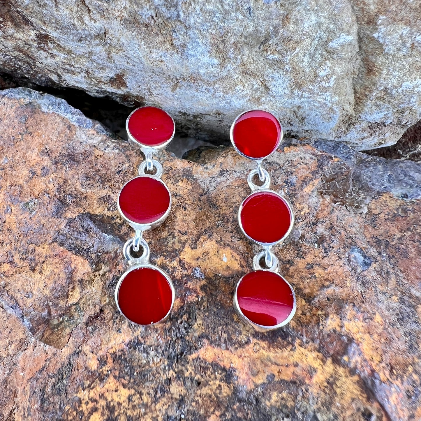 Red circular earrings with silver accents on a stone background