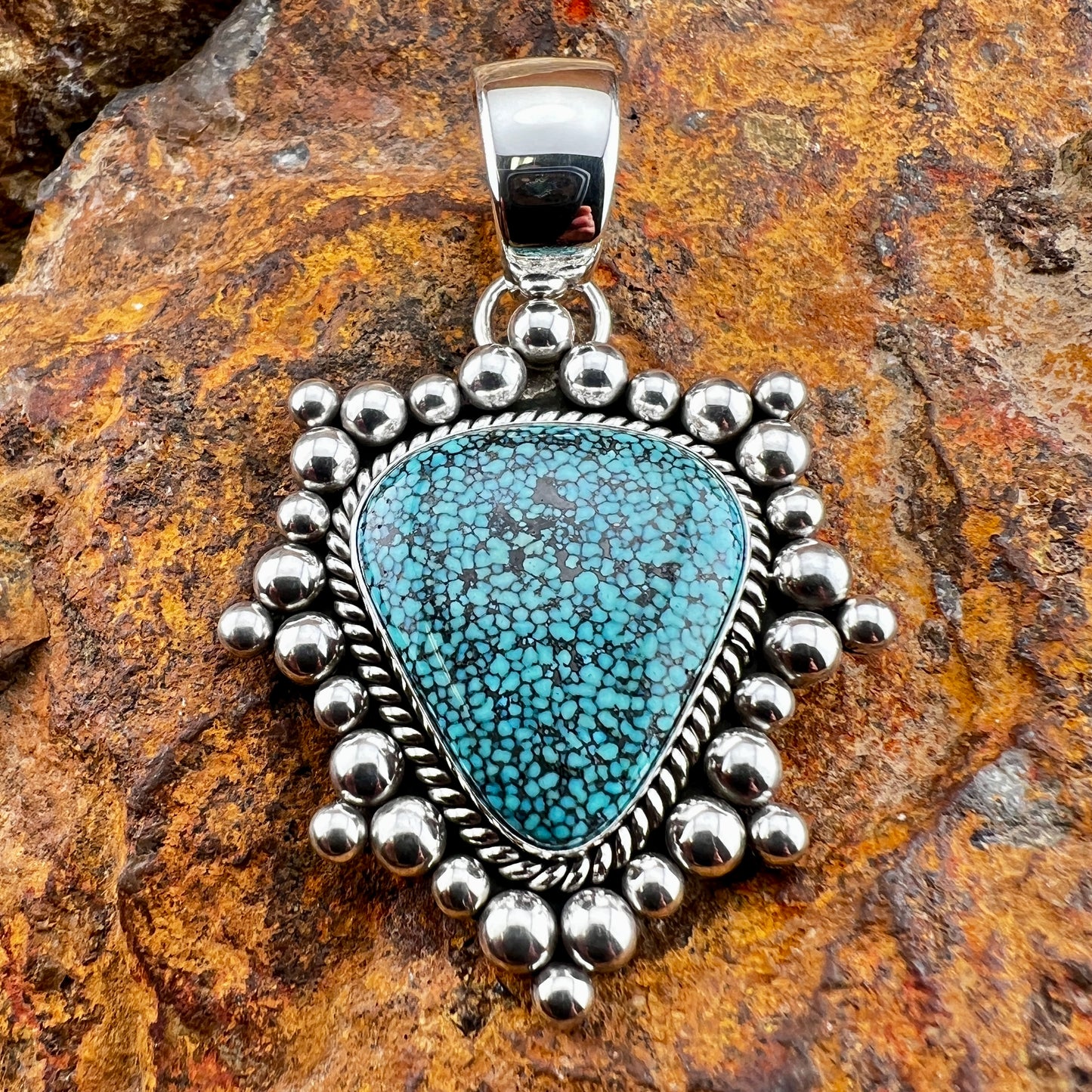 Turquoise pendant with silver beaded border on a stone background