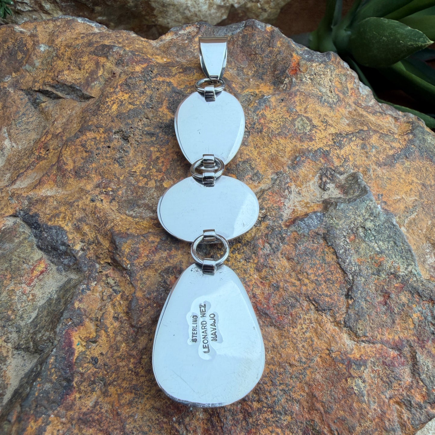 Back of a silver necklace pendant with stamping on it; LEONARD NEZ, NAVAJO, STERLING