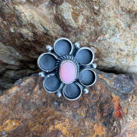 Silver flower shaped ring with a pink stone on a rocky surface