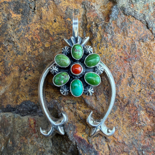 Silver pendant with green and red stones on a stone background