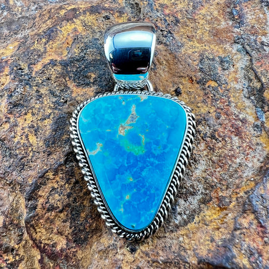 Turquoise stone pendant with silver setting on a textured stone background