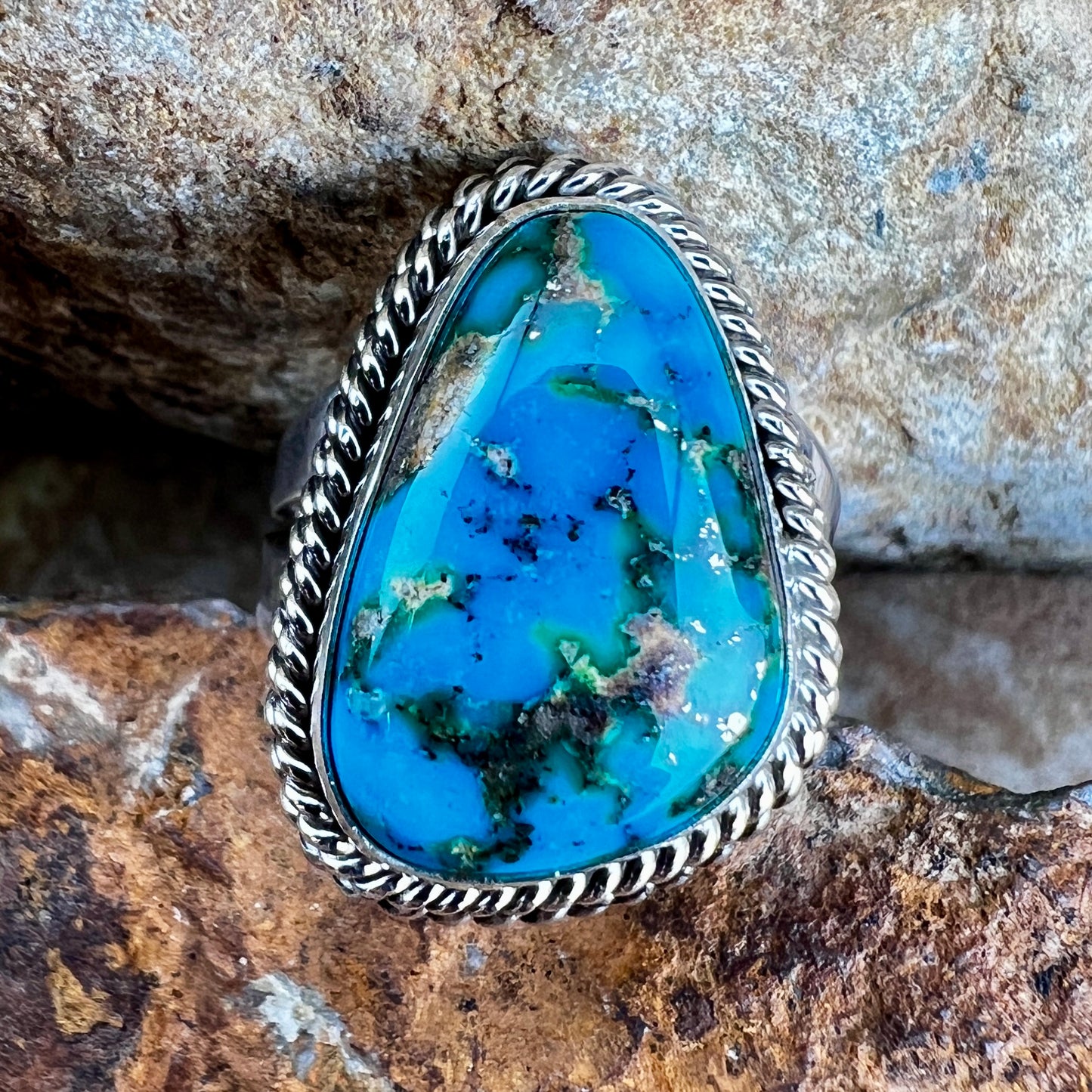 Turquoise stone with silver frame on a rock background