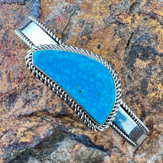 Turquoise stone bracelet with silver band on a textured stone background