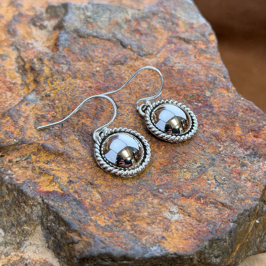 dome earrings with a twisted rope border by artie yellowhorse. they rest on a rocky surface