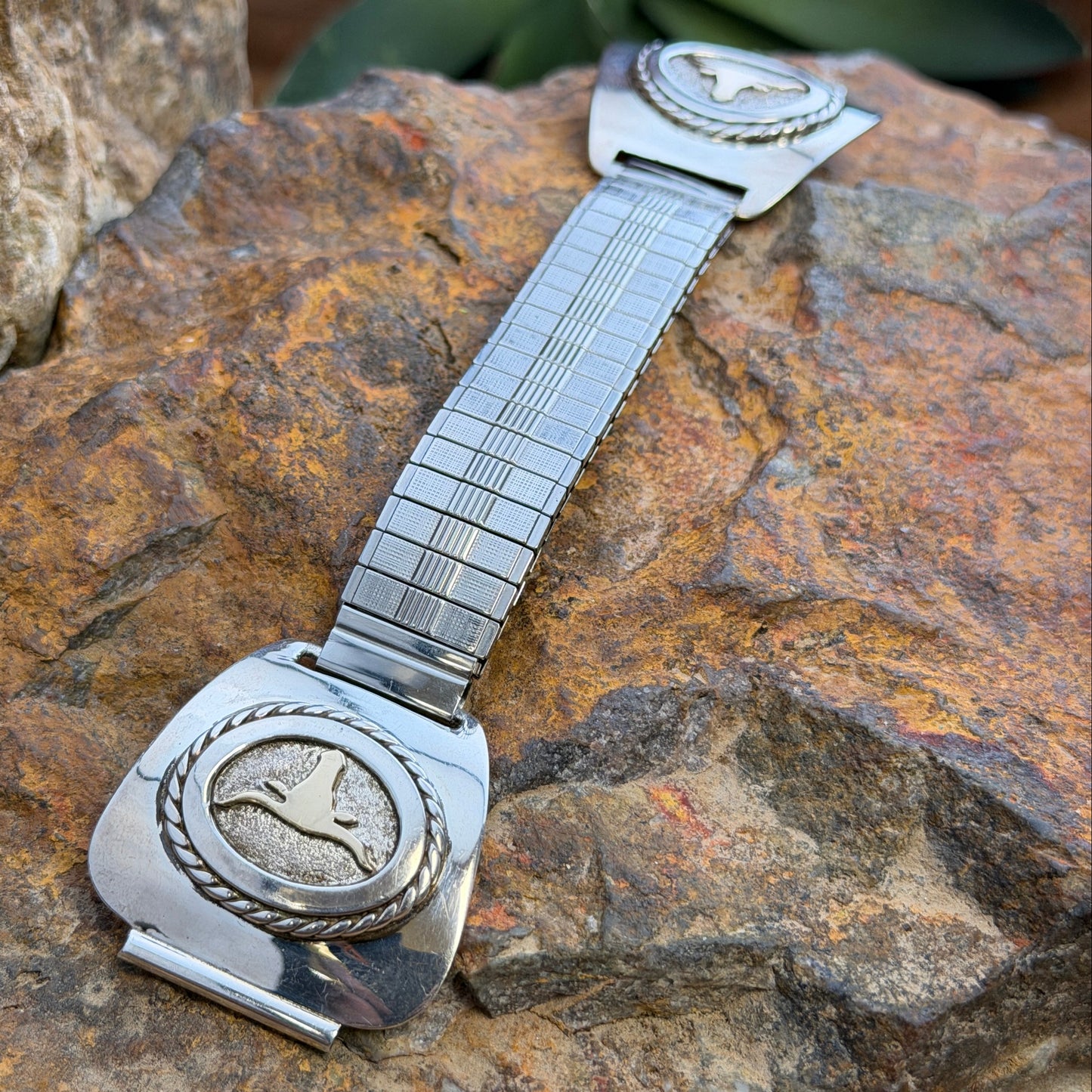 A sterling silver and 14k gold watch band decorative featuring a bull skull motif, displayed on a textured tan branch with a natural outdoor background.