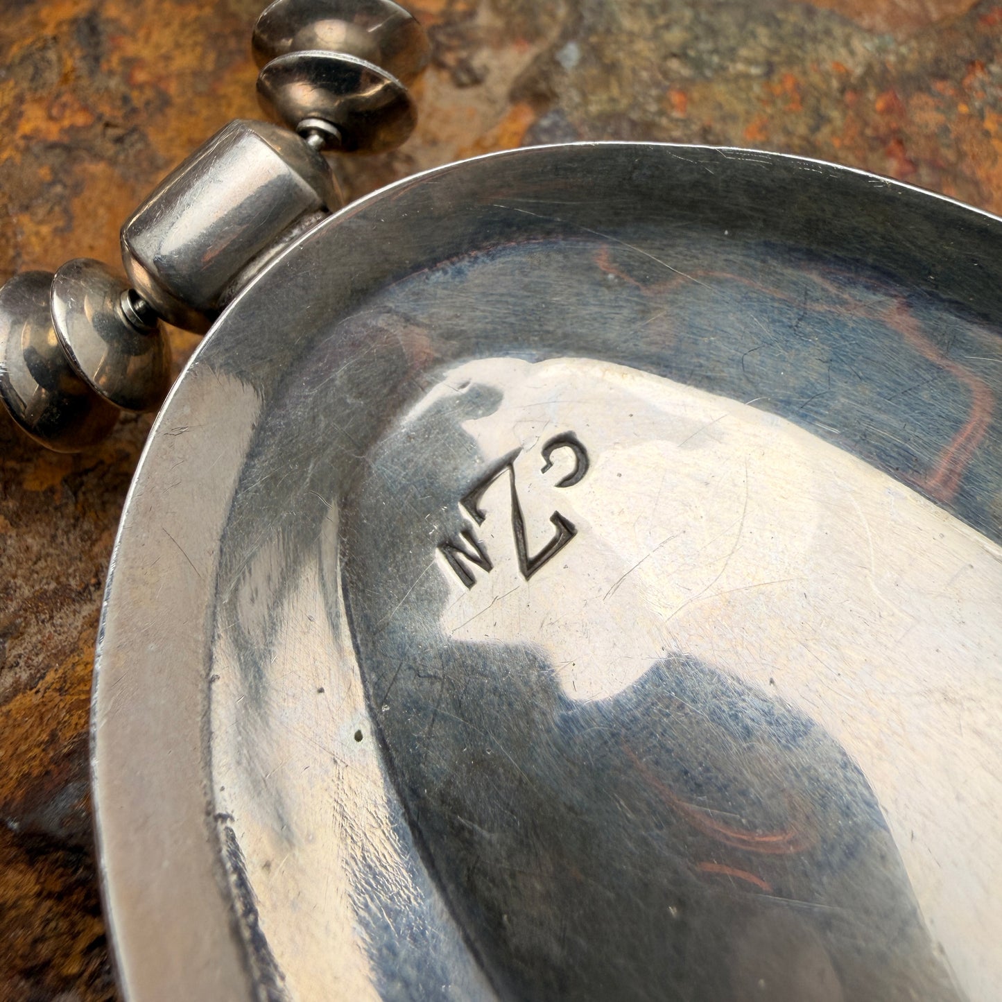 Close-up of a silver pendant with engraved initials GZN on a textured surface