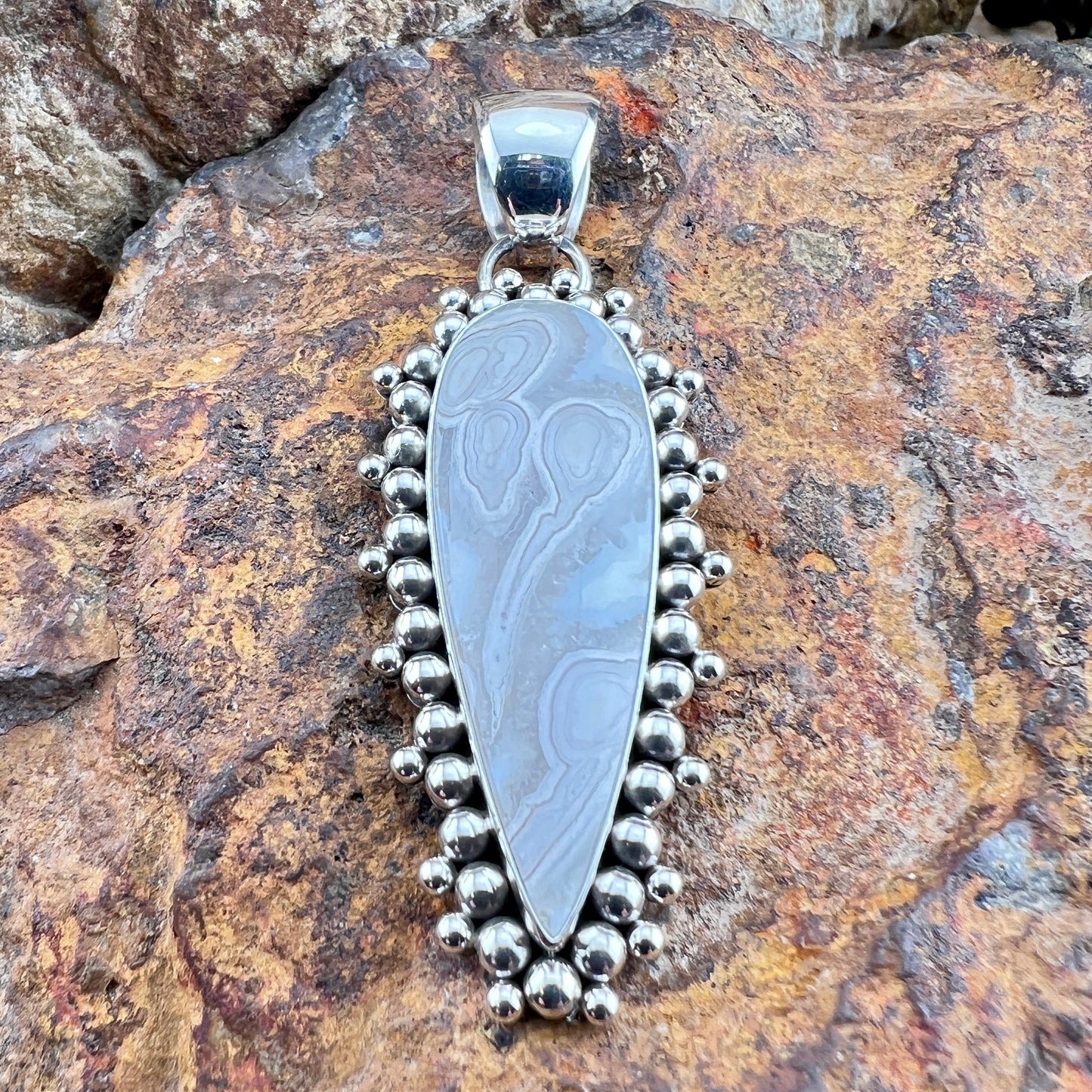 Silver pendant with intricate design on a rocky surface