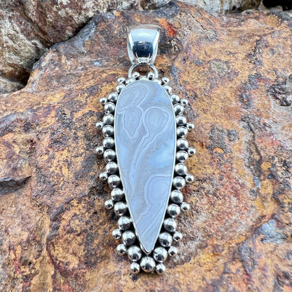 Silver pendant with intricate design on a rocky surface