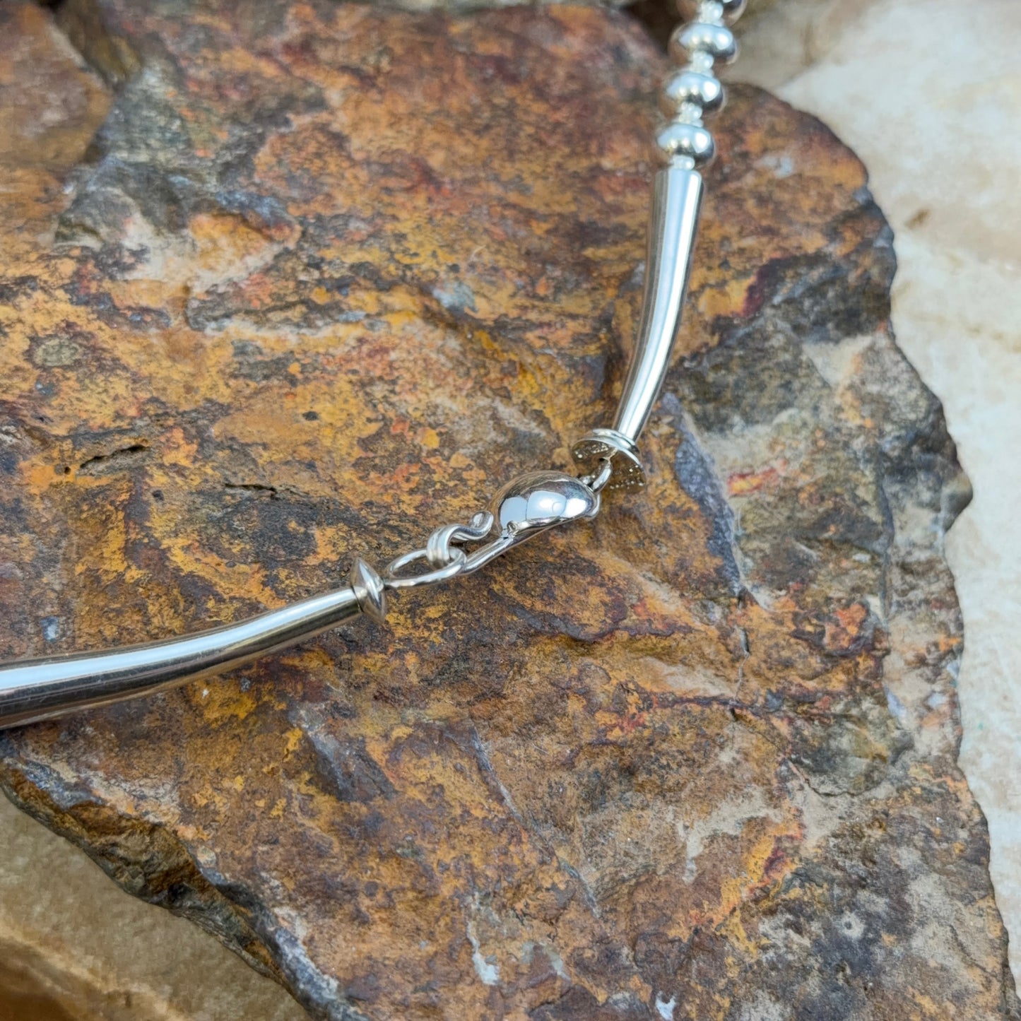 A close-up of a silver-toned beaded chain necklace draped over a textured brown and gold rock surface.