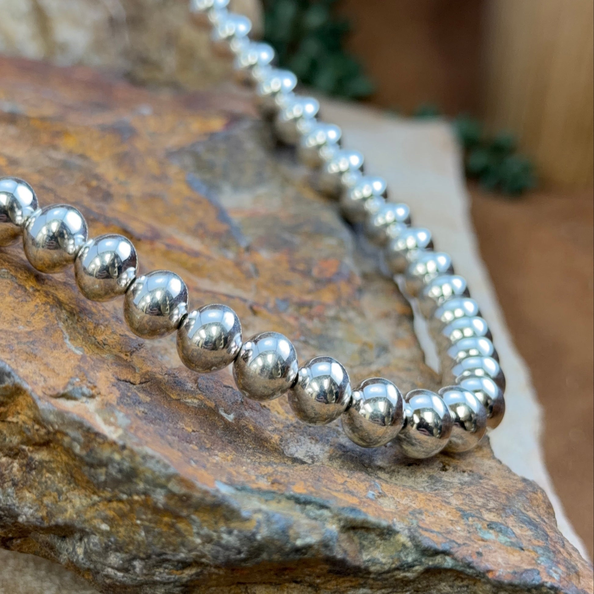 A close-up of a silver beaded necklace draped over a textured brown and tan stone surface.