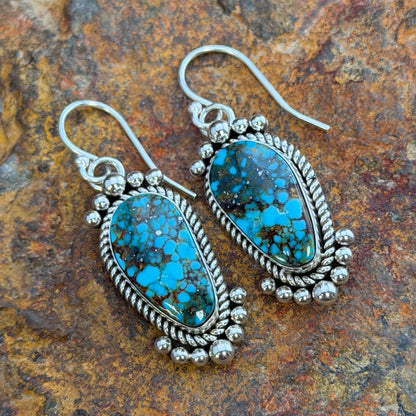 Kingman Turquoise Dangle Earrings by Artie Yellowhorse - flat lay on rock showing free-form turquoise cabochons and silverwork detail