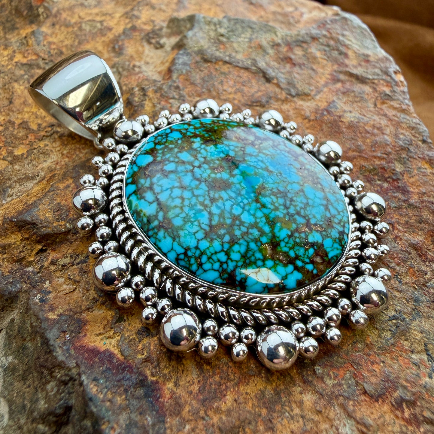 Kingman Turquoise Oval Pendant by Artie Yellowhorse - angled view showing twisted rope border and graduated silver bead surround