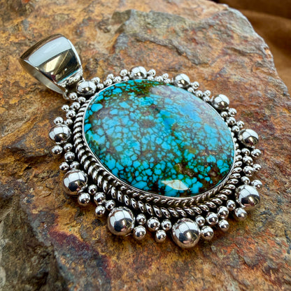 Kingman Turquoise Oval Pendant by Artie Yellowhorse - angled view showing twisted rope border and graduated silver bead surround