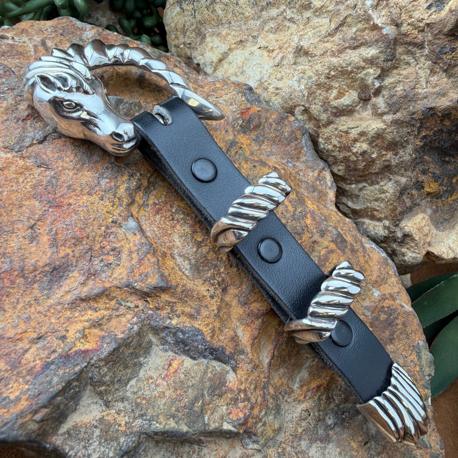 Black leather belt with silver metal buckle on a rocky surface