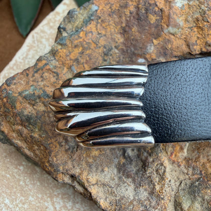Silver belt buckle on a black belt against a stone background