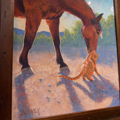 A framed painting depicting a brown horse bending down to an orange cat in a sunlit outdoor scene, with visible wooden frame edges and a signature in the lower left.