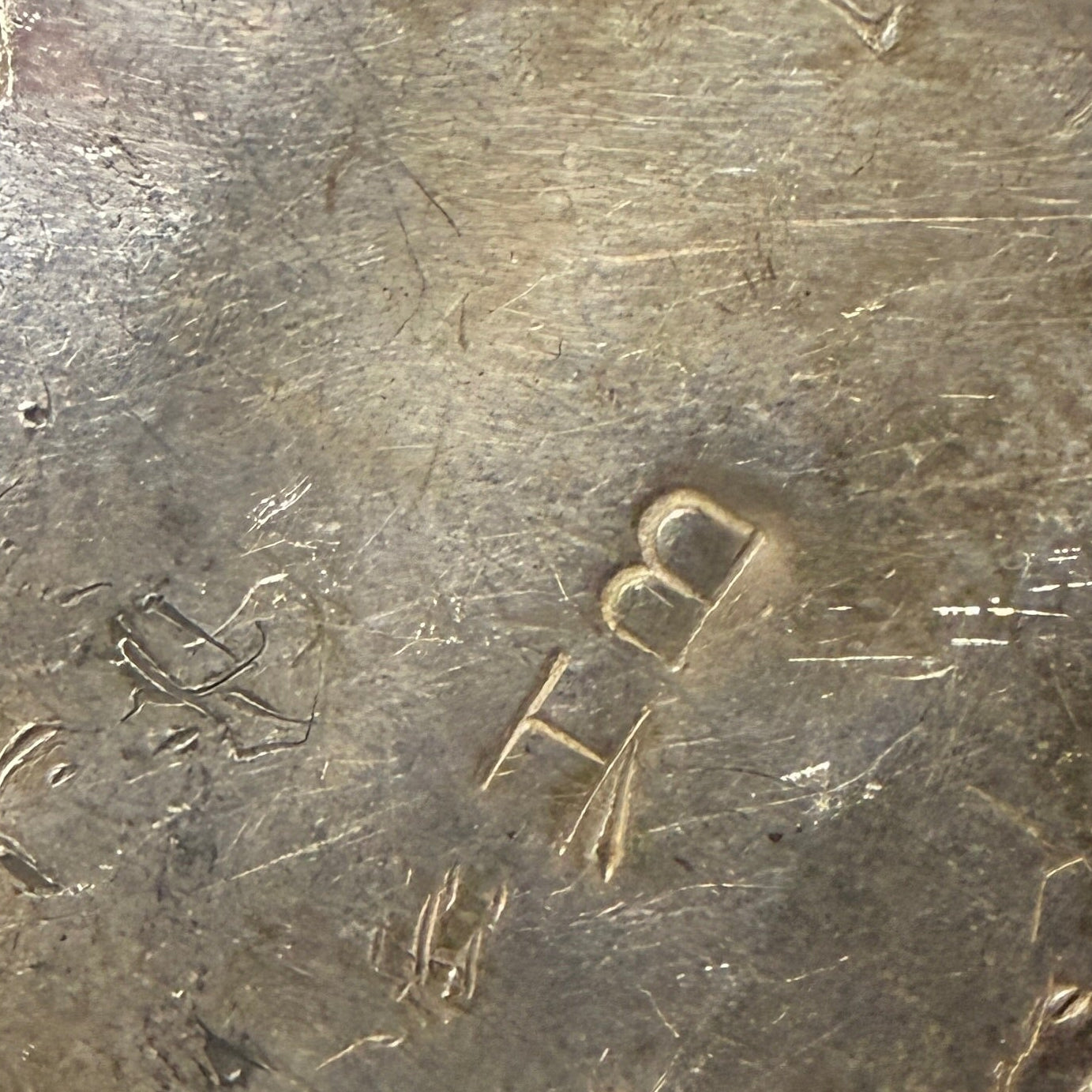 A close-up of a worn metal object with engraved hallmark "BH"