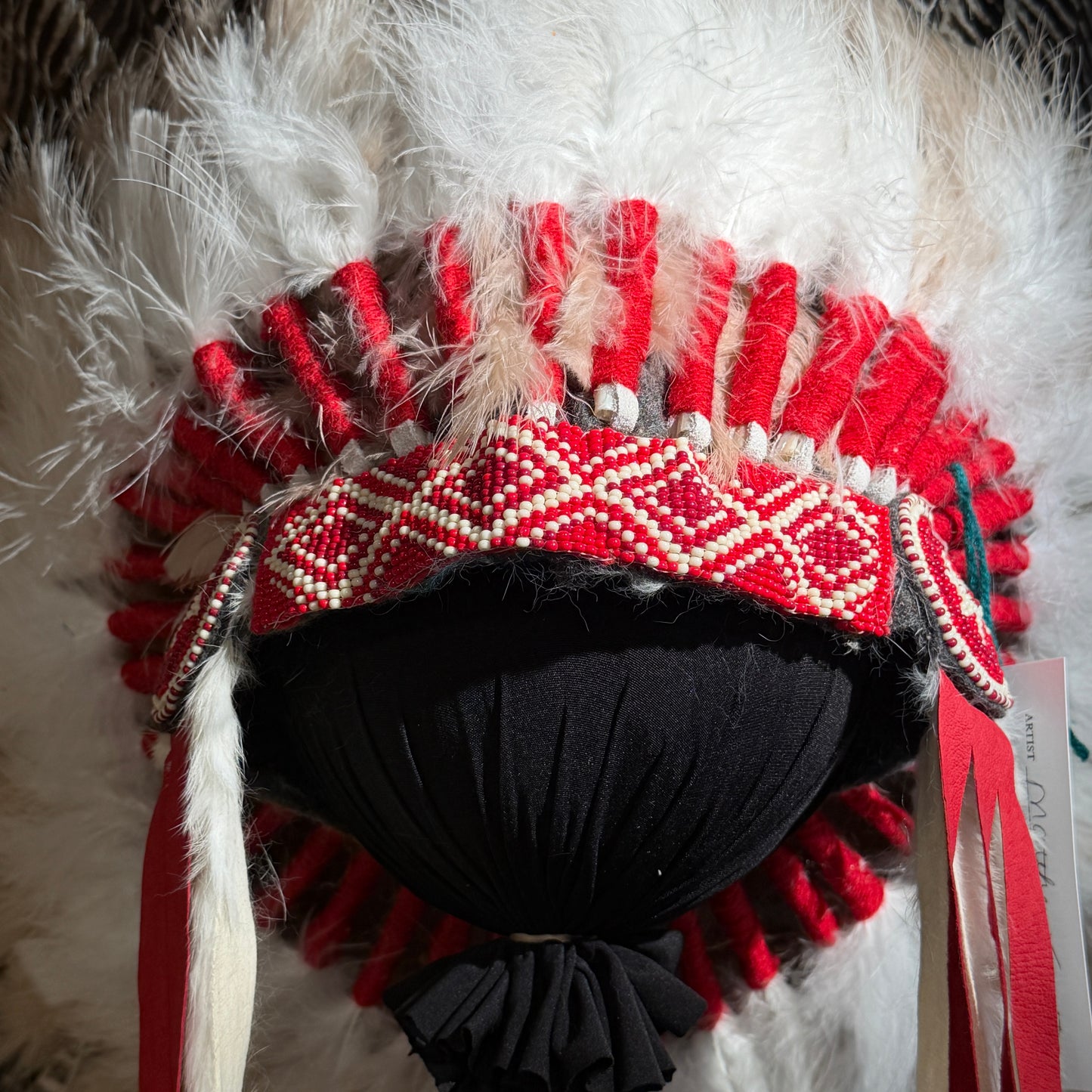 Close-up of a Native American headdress with red and white patterns on a black background.