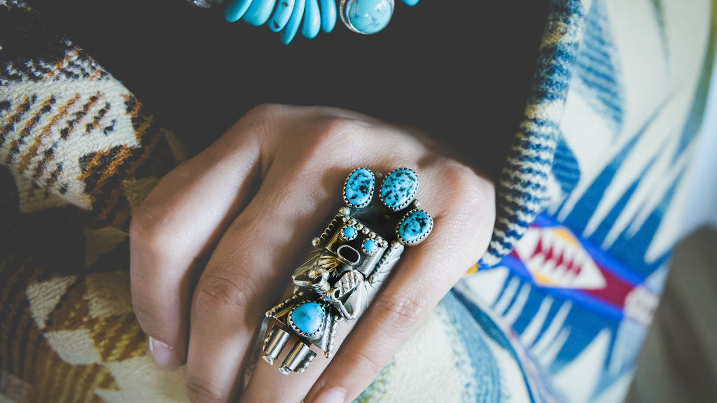 Hand wearing multiple turquoise and silver rings on a patterned fabric background