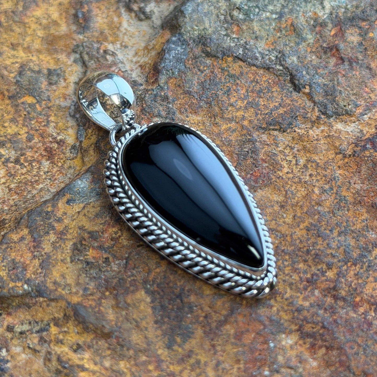 Black Onyx Pendant by Artie Yellowhorse - angled view on rock showing deep gloss finish and twisted rope setting