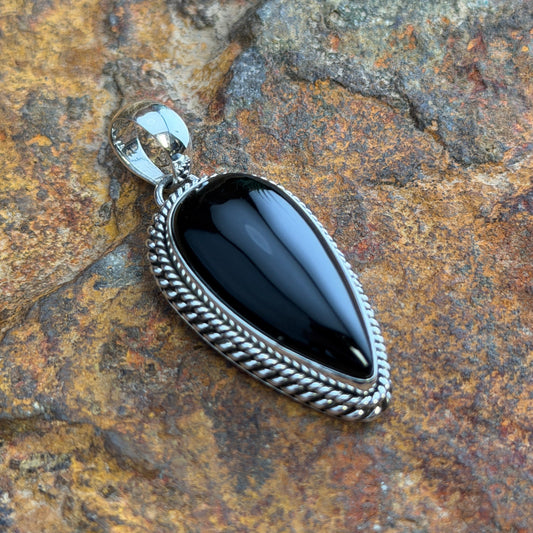 Black Onyx Pendant by Artie Yellowhorse - angled view on rock showing deep gloss finish and twisted rope setting