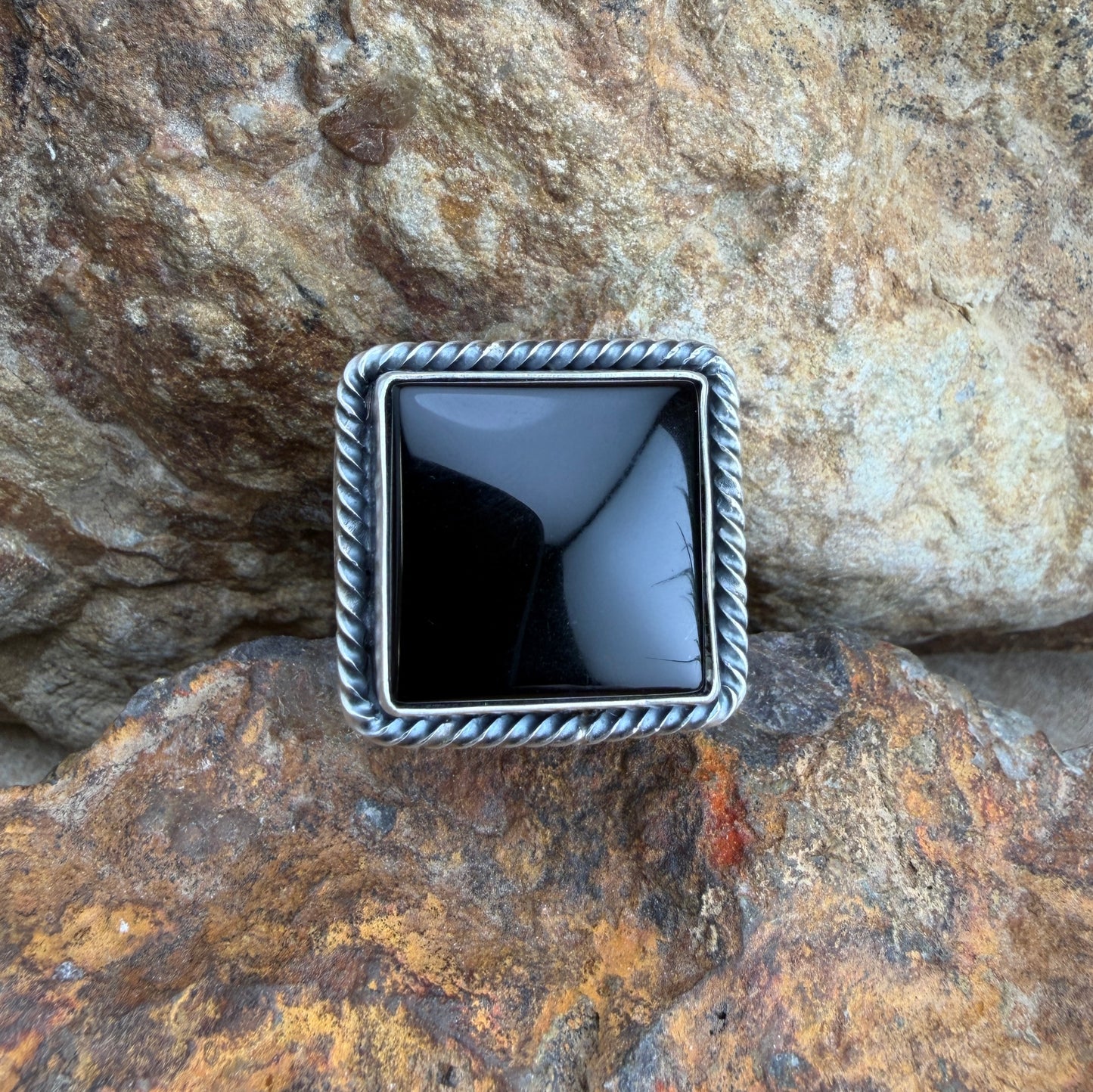 Square silver ring with black stone on a rocky surface