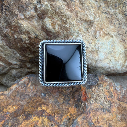 Square silver ring with black stone on a rocky surface
