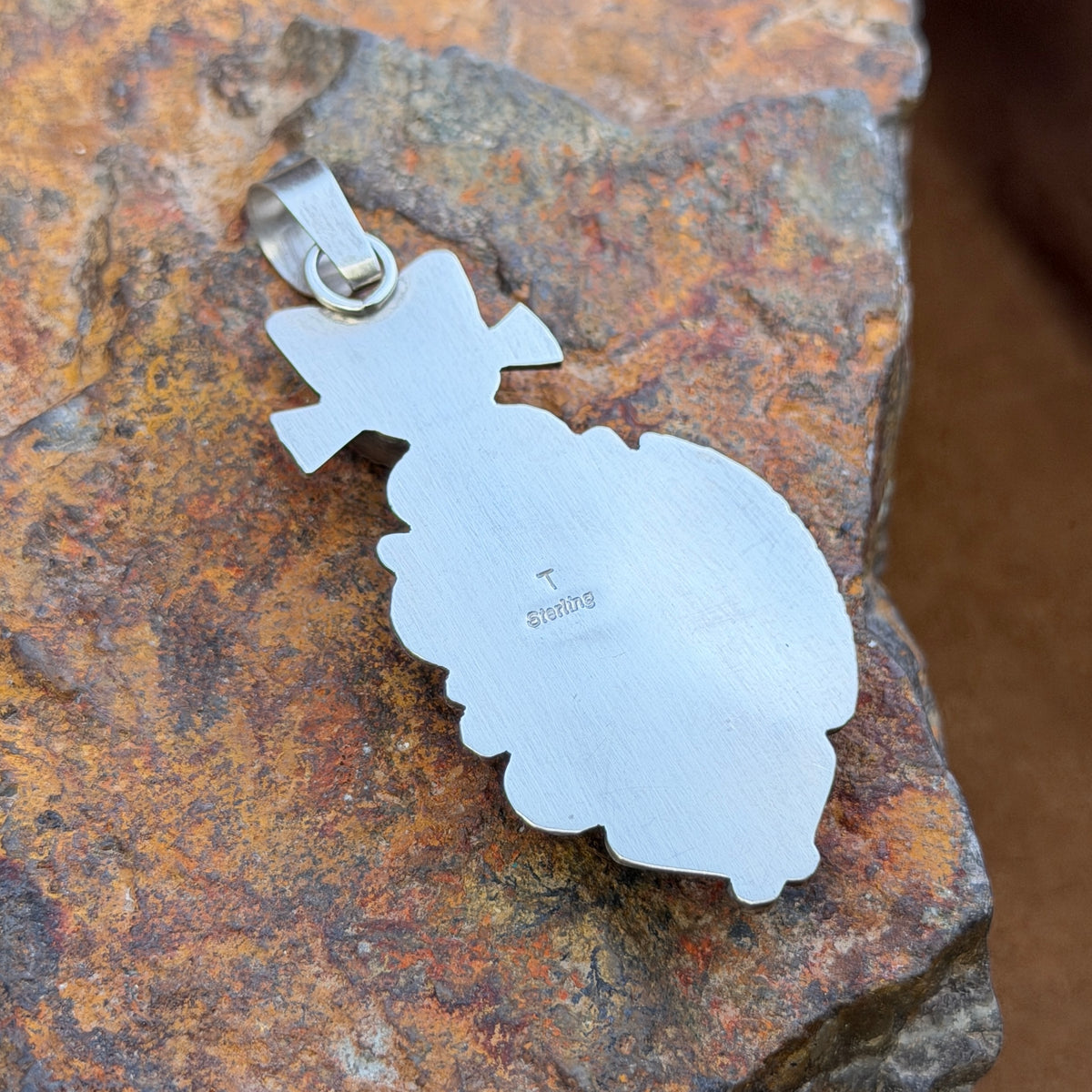 A cat pendant that head is made of black onyx stone, and body is made of an orange-yellow bumble bee jasper stone. silver work defines the cats silhouette. by mary tso. This picture is the reverse side showcasing the hallmark