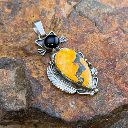 A cat pendant that head is made of black onyx stone, and body is made of an orange-yellow bumble bee jasper stone. silver work defines the cats silhouette. by mary tso