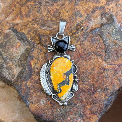 A cat pendant that head is made of black onyx stone, and body is made of an orange-yellow bumble bee jasper stone. silver work defines the cats silhouette. by mary tso