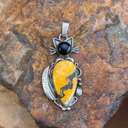 A cat pendant that head is made of black onyx stone, and body is made of an orange-yellow bumble bee jasper stone. silver work defines the cats silhouette. by mary tso