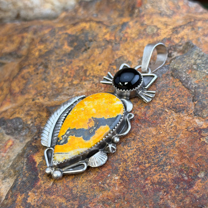 A cat pendant that head is made of black onyx stone, and body is made of an orange-yellow bumble bee jasper stone. silver work defines the cats silhouette. by mary tso
