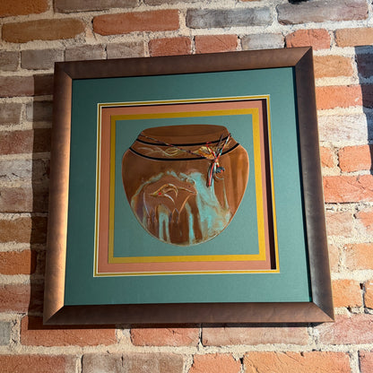 Framed artwork of a ceramic jar with a decorative element on a brick wall background
