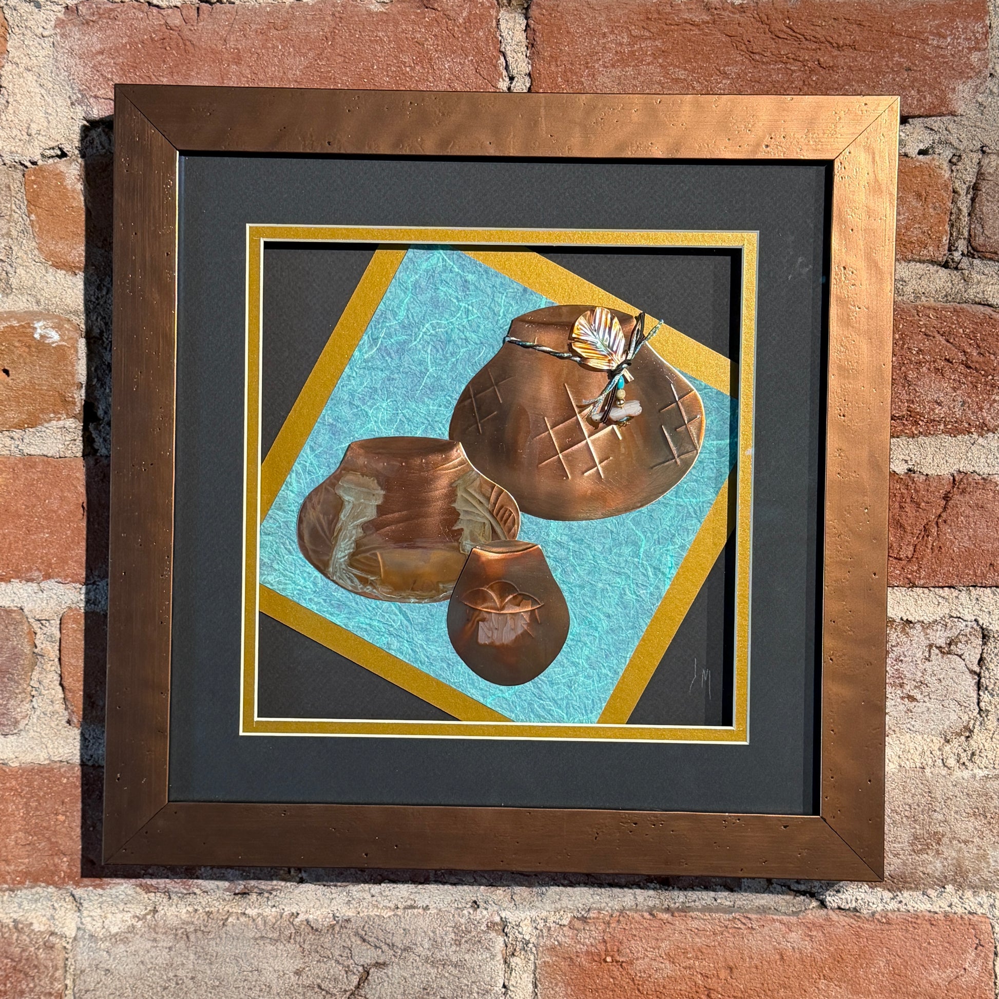 Framed artwork of two bronze pots on a textured blue background, leaning against a brick wall.