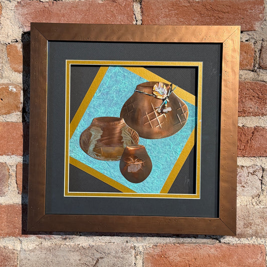 Framed artwork of two bronze pots on a textured blue background, leaning against a brick wall.