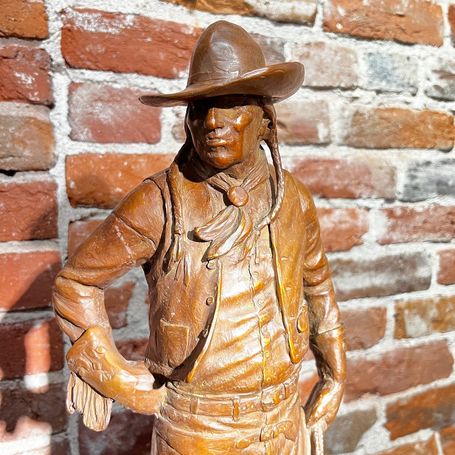 Bronze statue of a cowboy against a brick wall