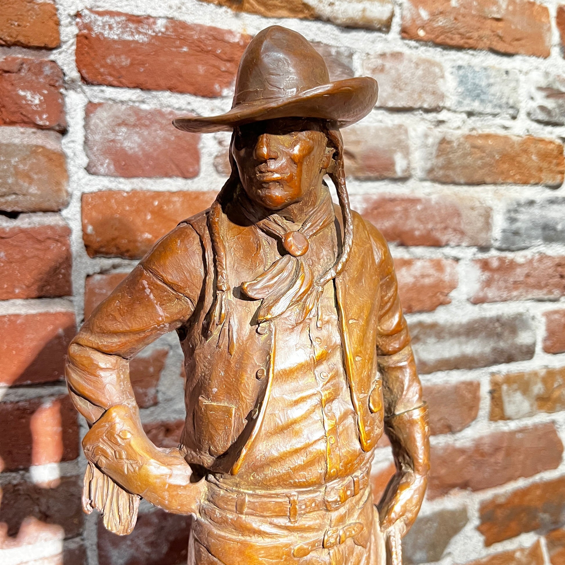 Bronze statue of a cowboy against a brick wall