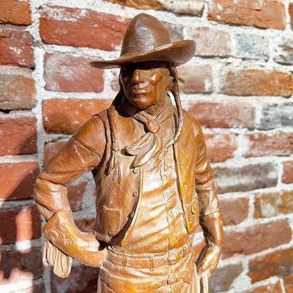 Bronze statue of a cowboy against a brick wall