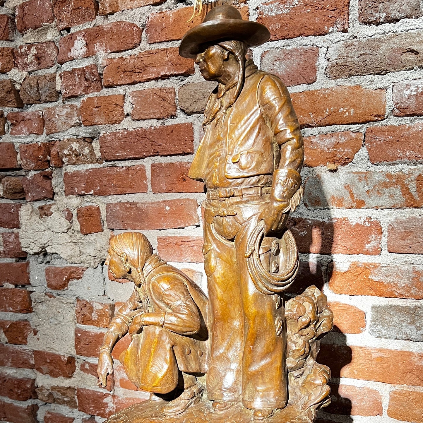 Bronze sculpture of a cowboy and horse on a wooden platform against a brick wall.