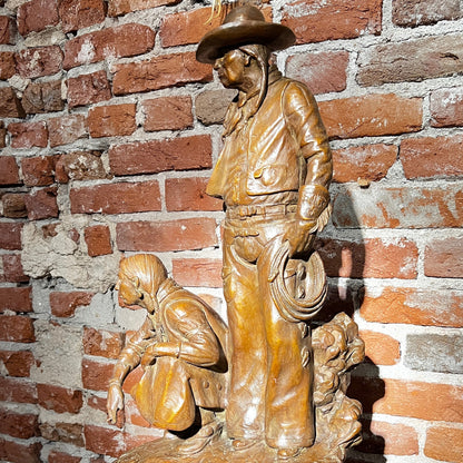 Bronze sculpture of a cowboy and horse on a wooden platform against a brick wall.
