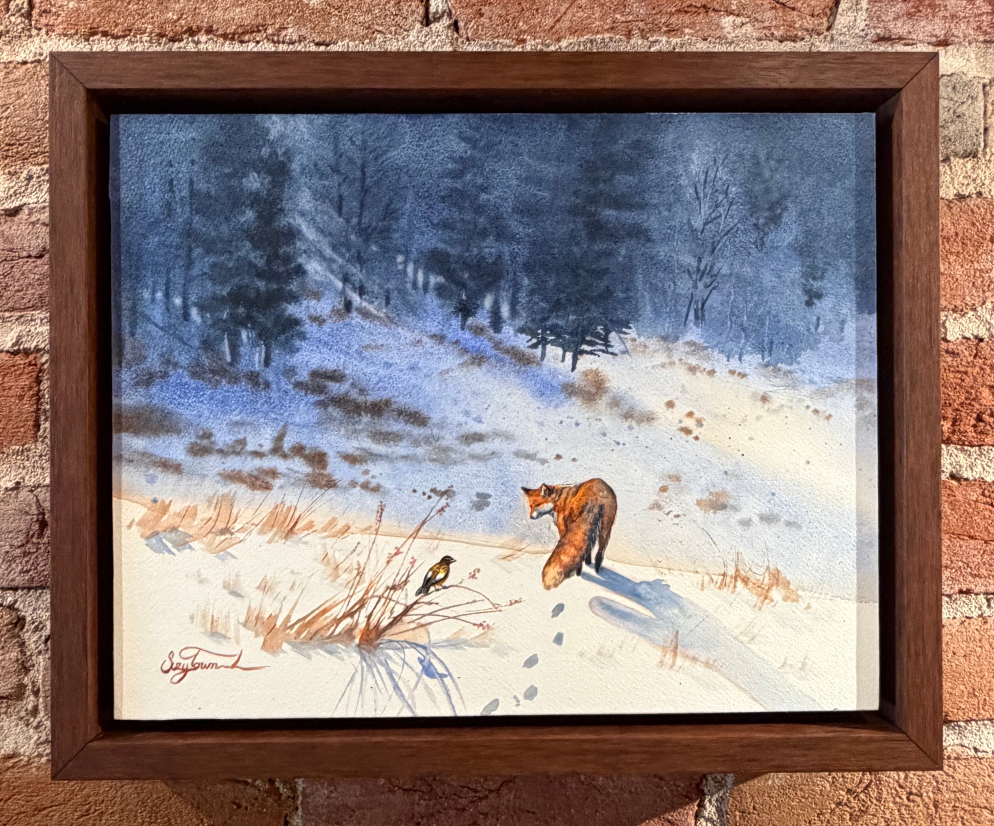 Framed painting of a fox in a snowy landscape on a brick wall.