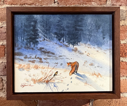 Framed painting of a fox in a snowy landscape on a brick wall.